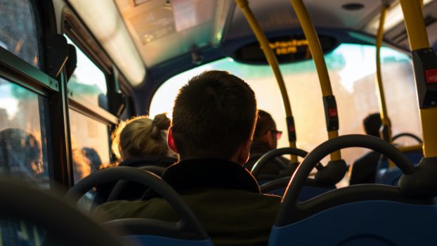 Decorative image: A silhouette of a man sitting on a bus facing forward. 